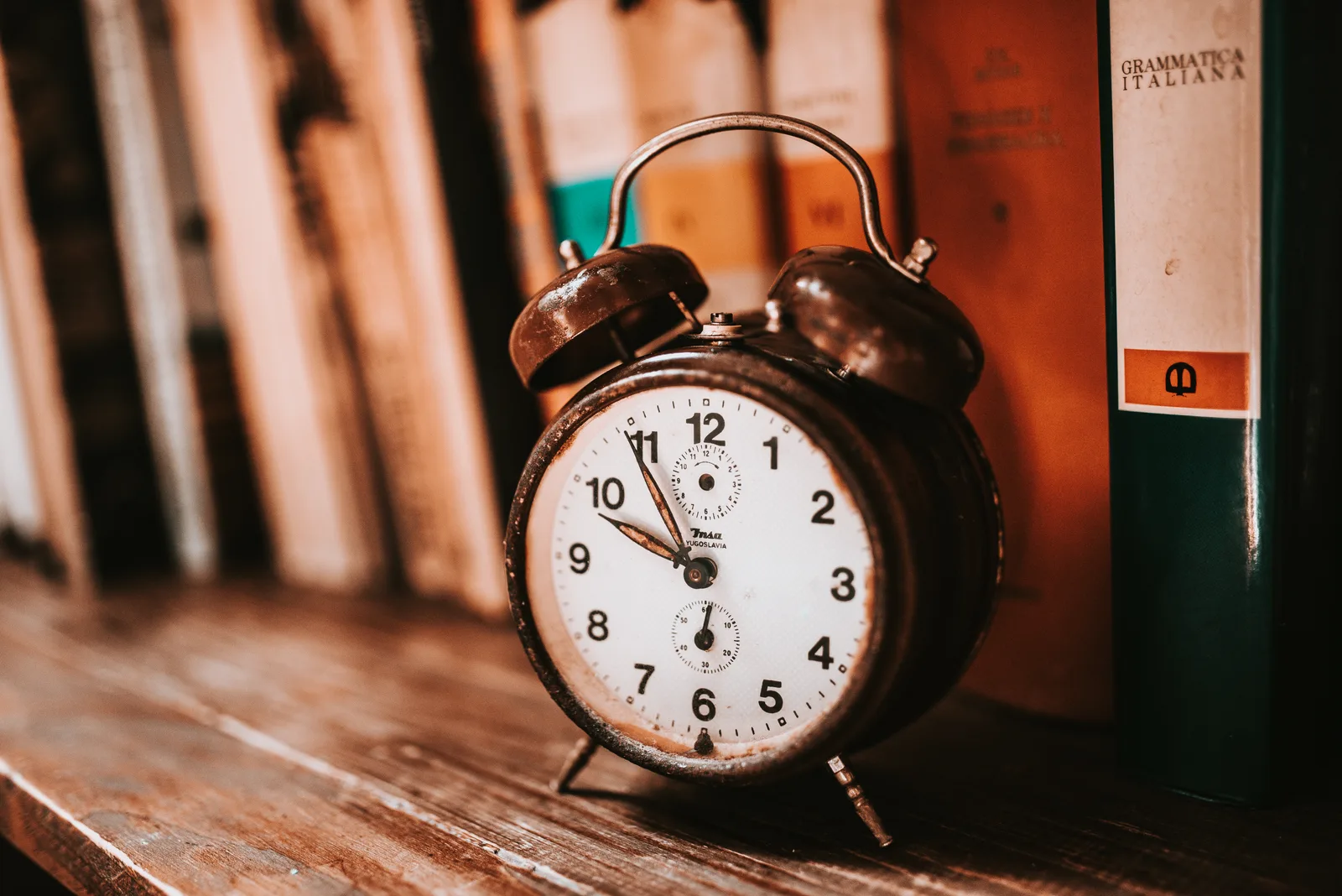 A vintage alarm clock on a wooden desk beside a row of books.